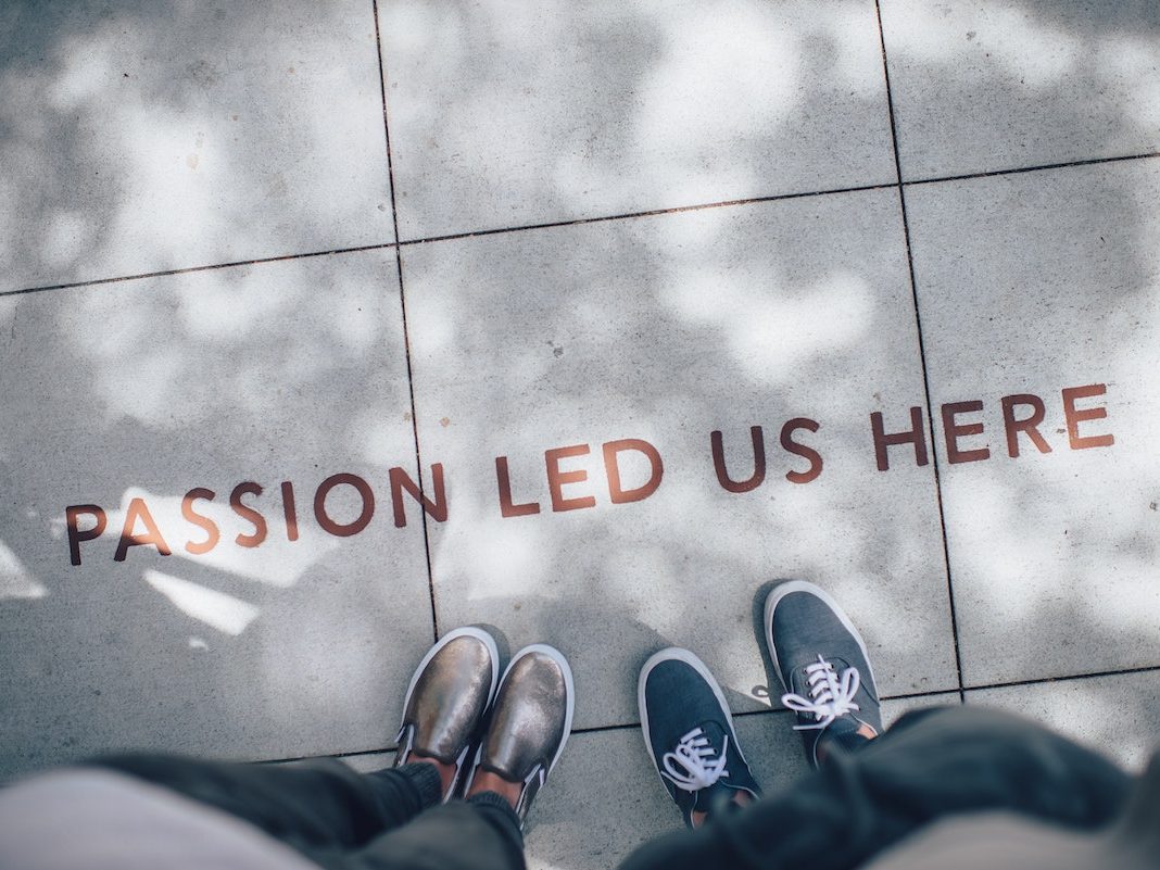 The words Passion led us here written on a sidewalk, two pairs of shoes beside them